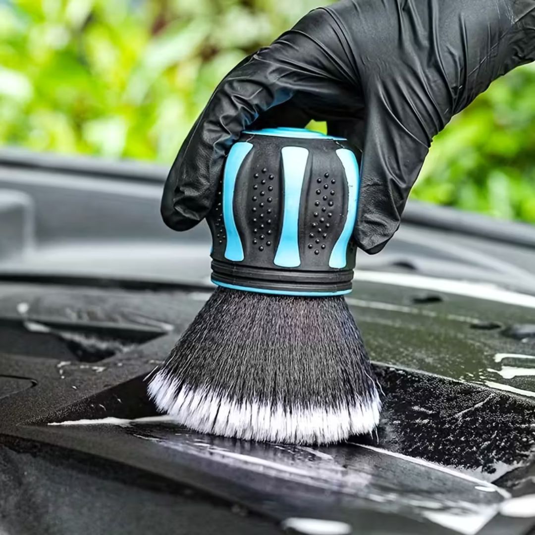 Car cleaning brush with black bristles and blue handle being used on a car hood.