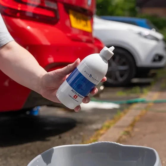 Person holding a bottle of Bilt Hamber auto-wash soap with cars in the background