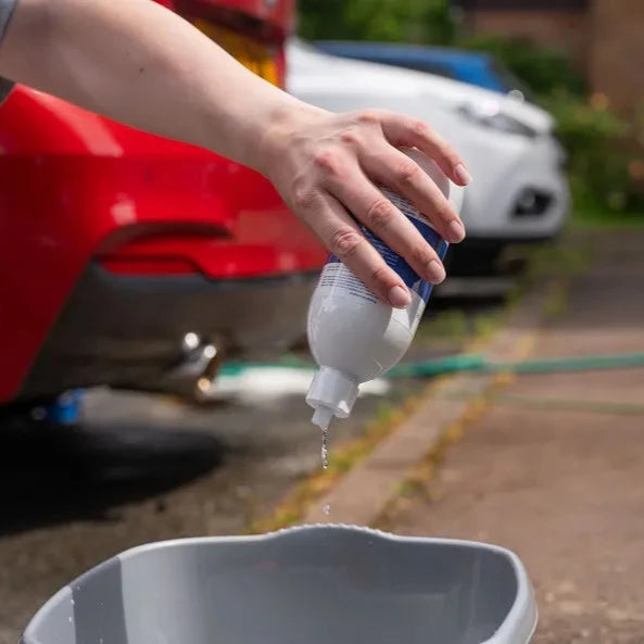 Person holding a bottle of bilt hamber auto-wash over a car wash bucket with cars in the background
