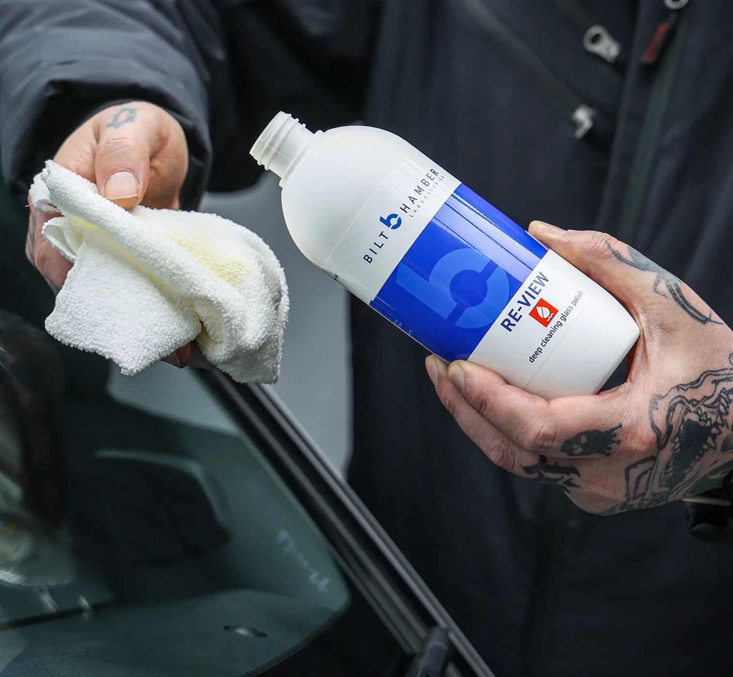 Person holding a bottle of Bilt Hamber Re-View glass polish product and a white cloth