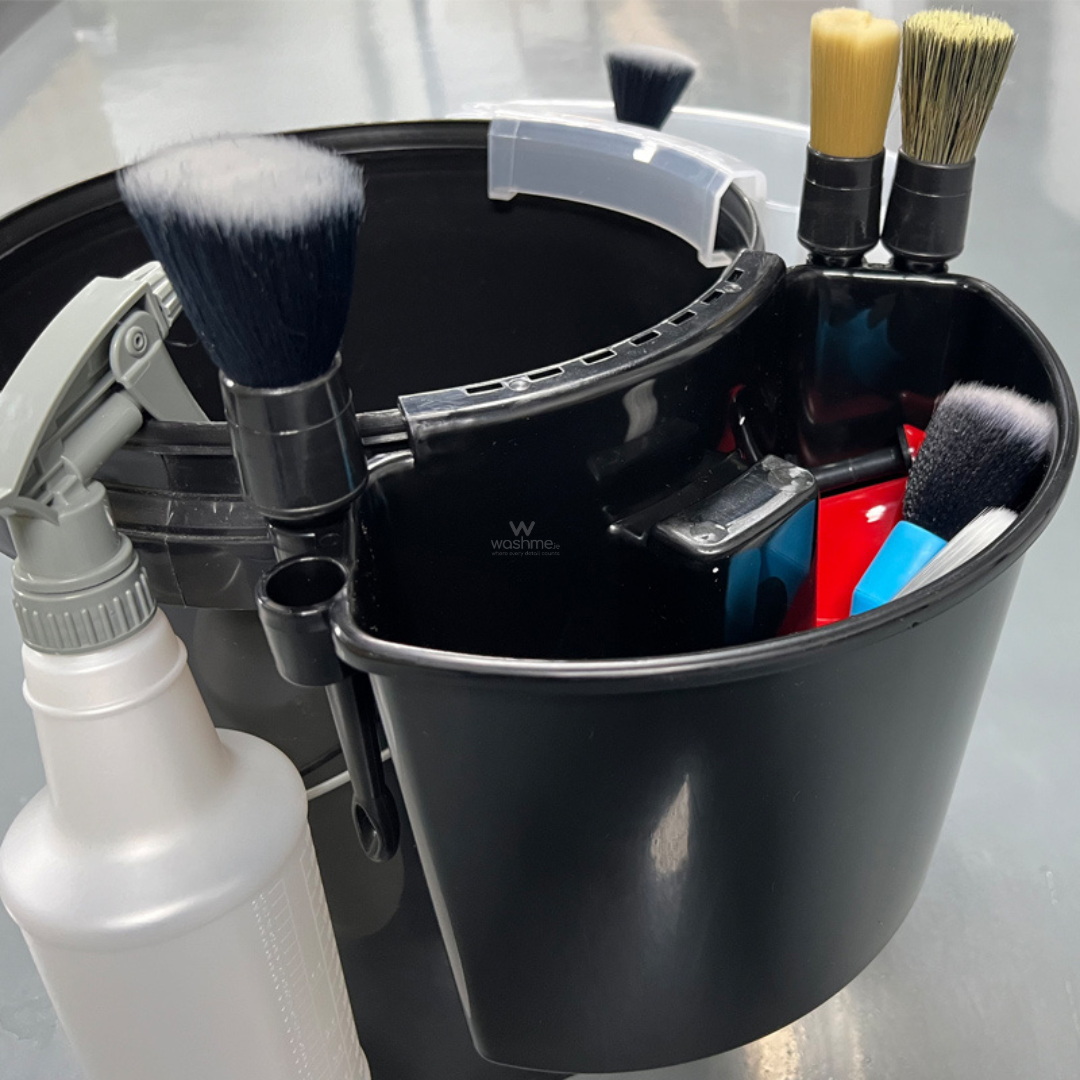 Black cleaning caddy with brushes, bottles, and tools on a gray background