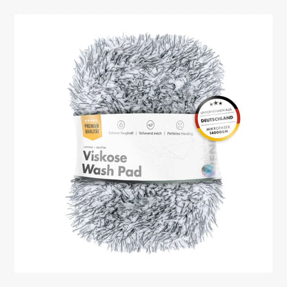 A fluffy gray and white shaggy Viskose Wash Pad with a white paper label band around it, photographed on a clean white background. A circular German quality badge is visible on the right side of the label.