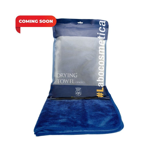 A blue Labocosmetica drying towel folded over its branded packaging, with a red 'COMING SOON' banner overlay in the top left corner.