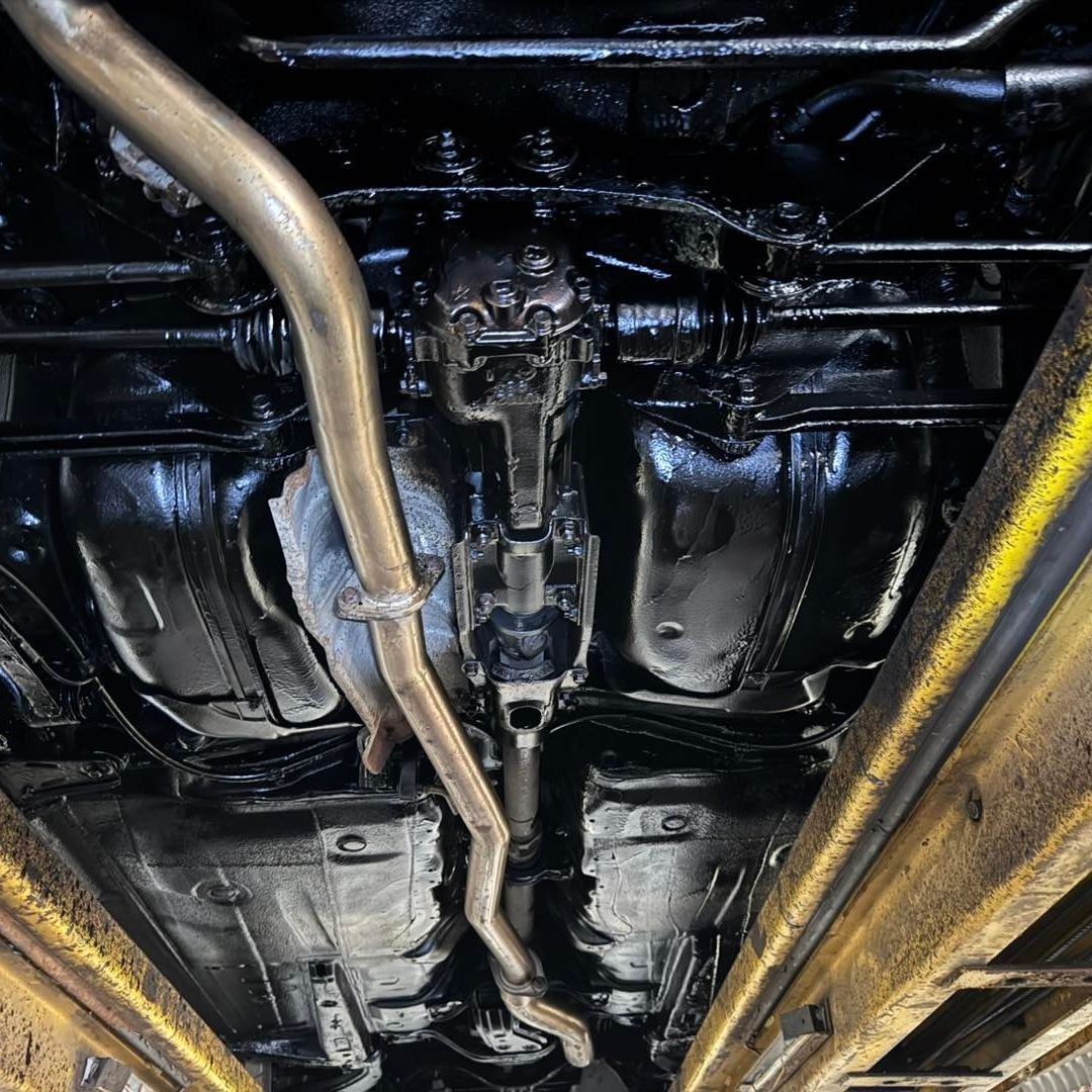 Bilt Hamber Dynax UB used on Undercarriage view of a vehicle on a yellow service lift, showing the exhaust system, suspension, and fuel system components.