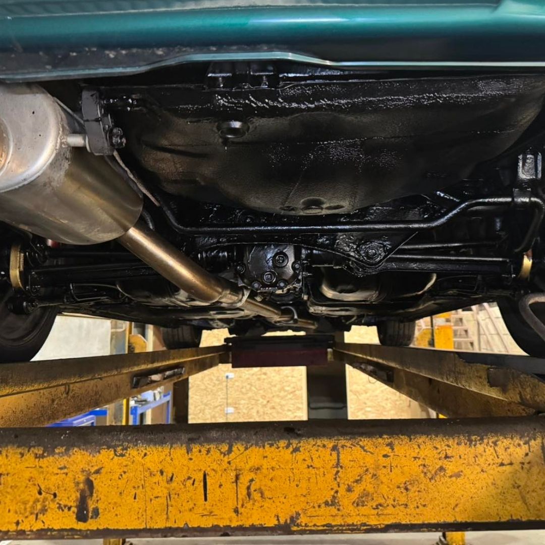 Bilt Hamber Dynax UB used on Undercarriage view of a vehicle on a yellow service lift, showing the exhaust system, suspension, and fuel system components.