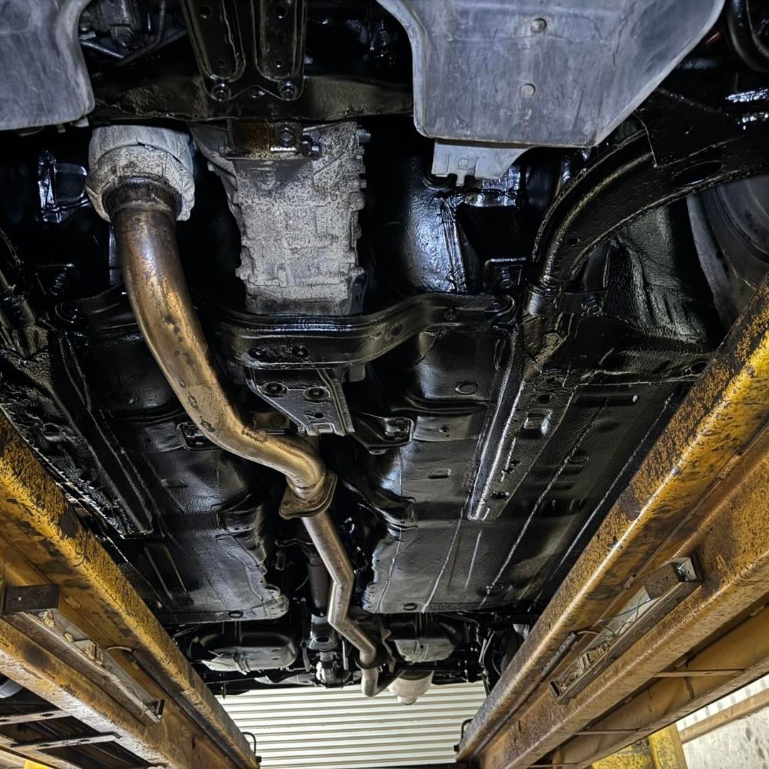 Bilt Hamber Dynax UB used on Undercarriage view of a vehicle on a yellow service lift, showing the exhaust system, suspension, and fuel system components.