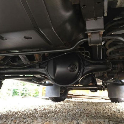 Close-up underside view of a black automotive differential and axle assembly mounted under a vehicle on a gravel surface. Painted with Bilt Hamber Dynax UB rust protection