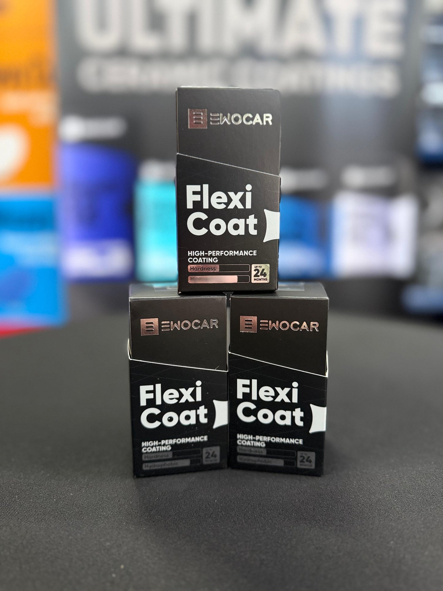 Three boxes of EWOCAR Flexi Coat on a dark surface with blurred colorful background