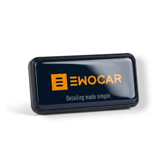 A glossy black rectangular EWOCAR air freshener  detailing product, likely a sponge block or applicator, featuring the orange and white EWOCAR logo and the tagline 'Detailing made simple.' on a clean white background.