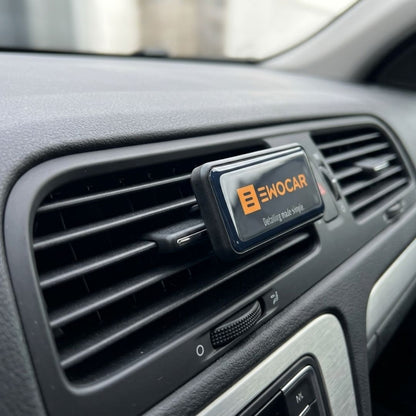 A black car air vent clip with the brand name 'EWOCAR' in orange and white, shown attached to a car dashboard air vent.