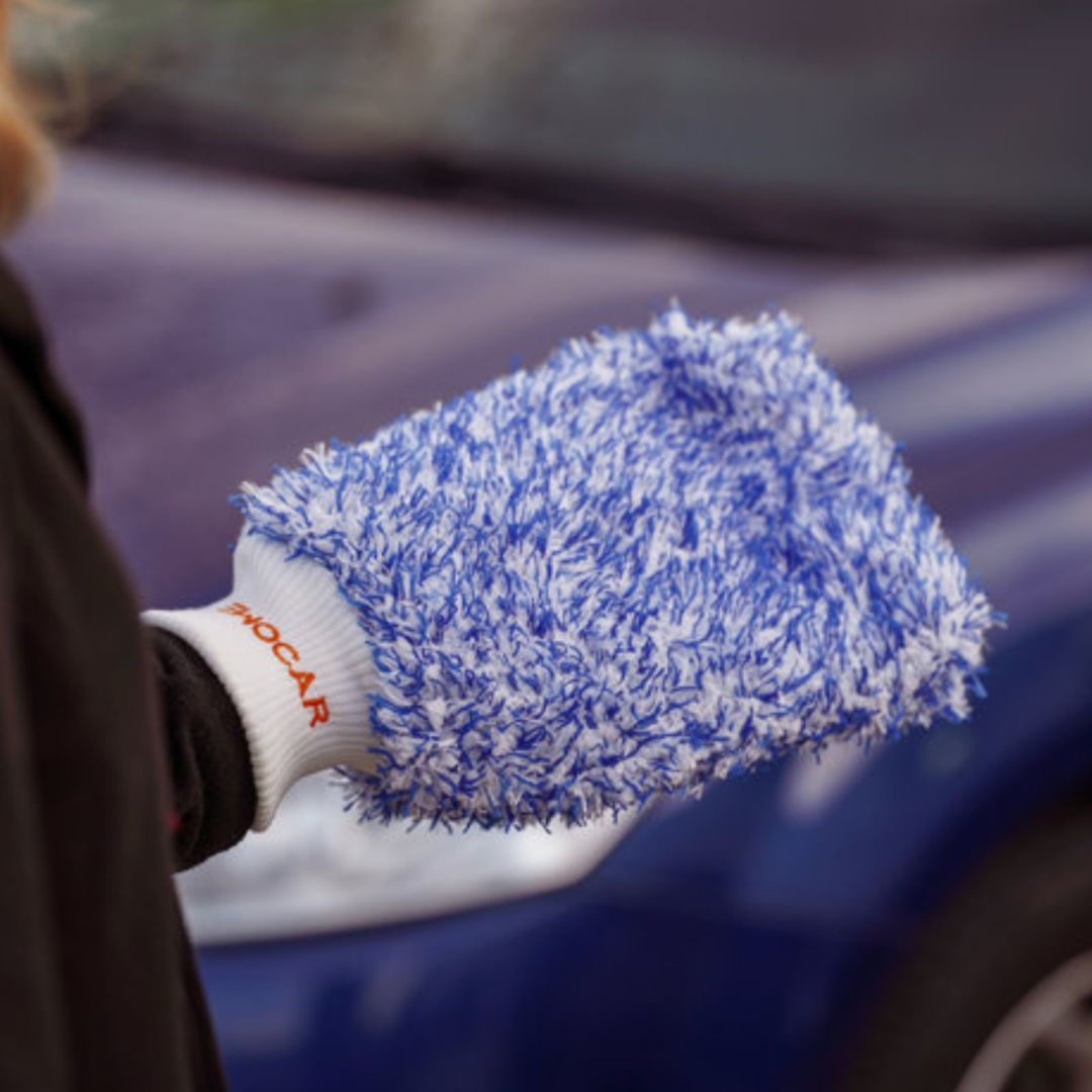 Car wash glove mitt with blue microfibre held in front of a car
