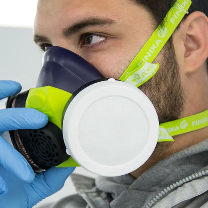 A close-up of a man wearing a dark blue and neon green Finaixa respirator mask with a white filter canister, wearing blue gloves and a gray jacket.