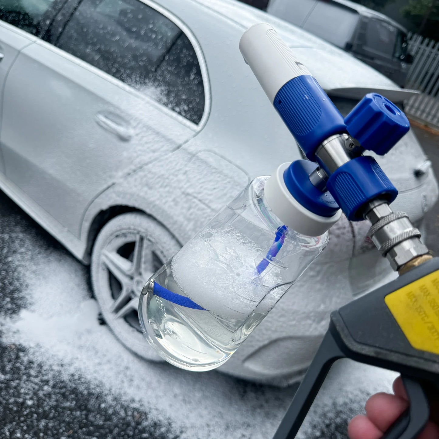 Car wash gun with soap bottle in front of a car