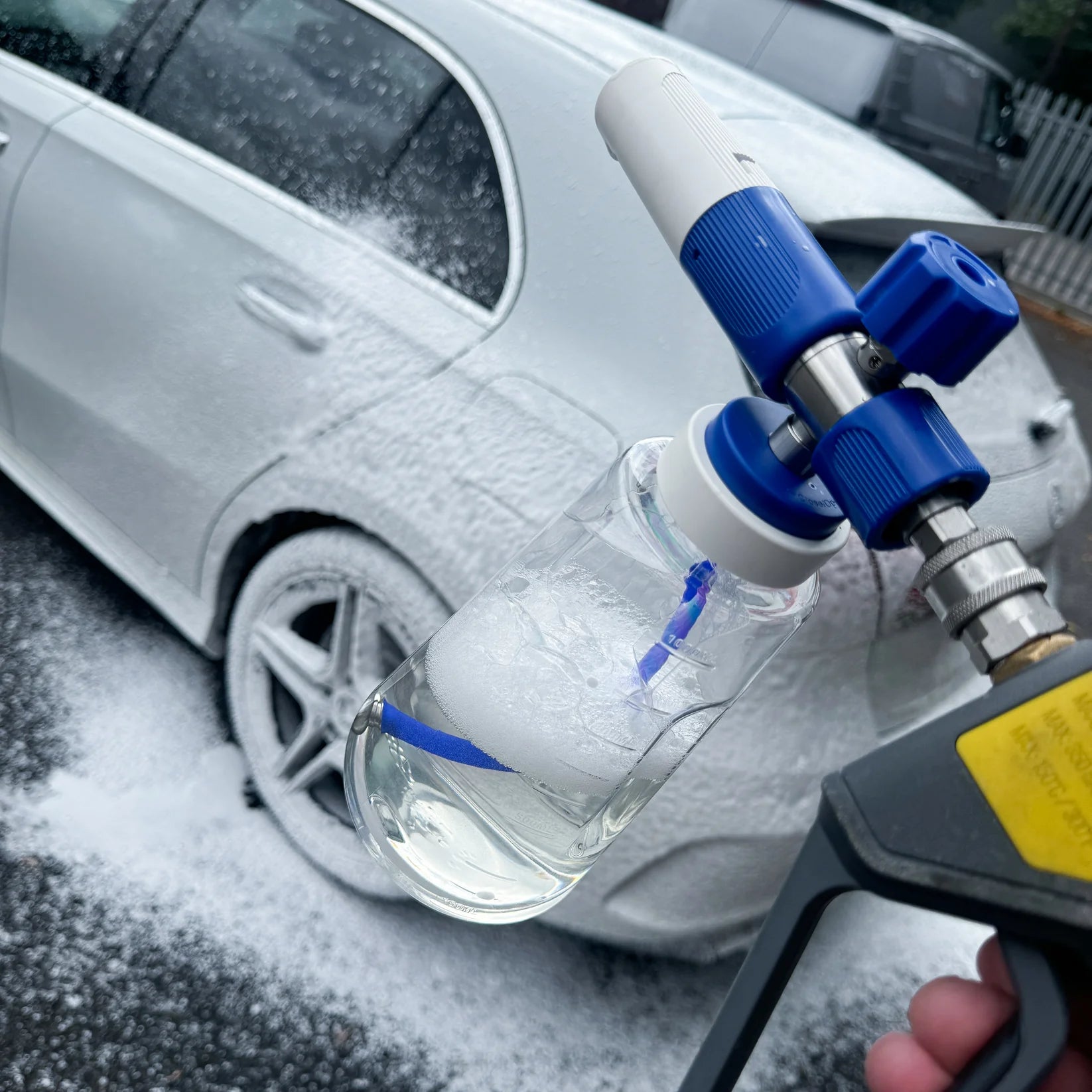 Car wash gun with soap bottle in front of a car