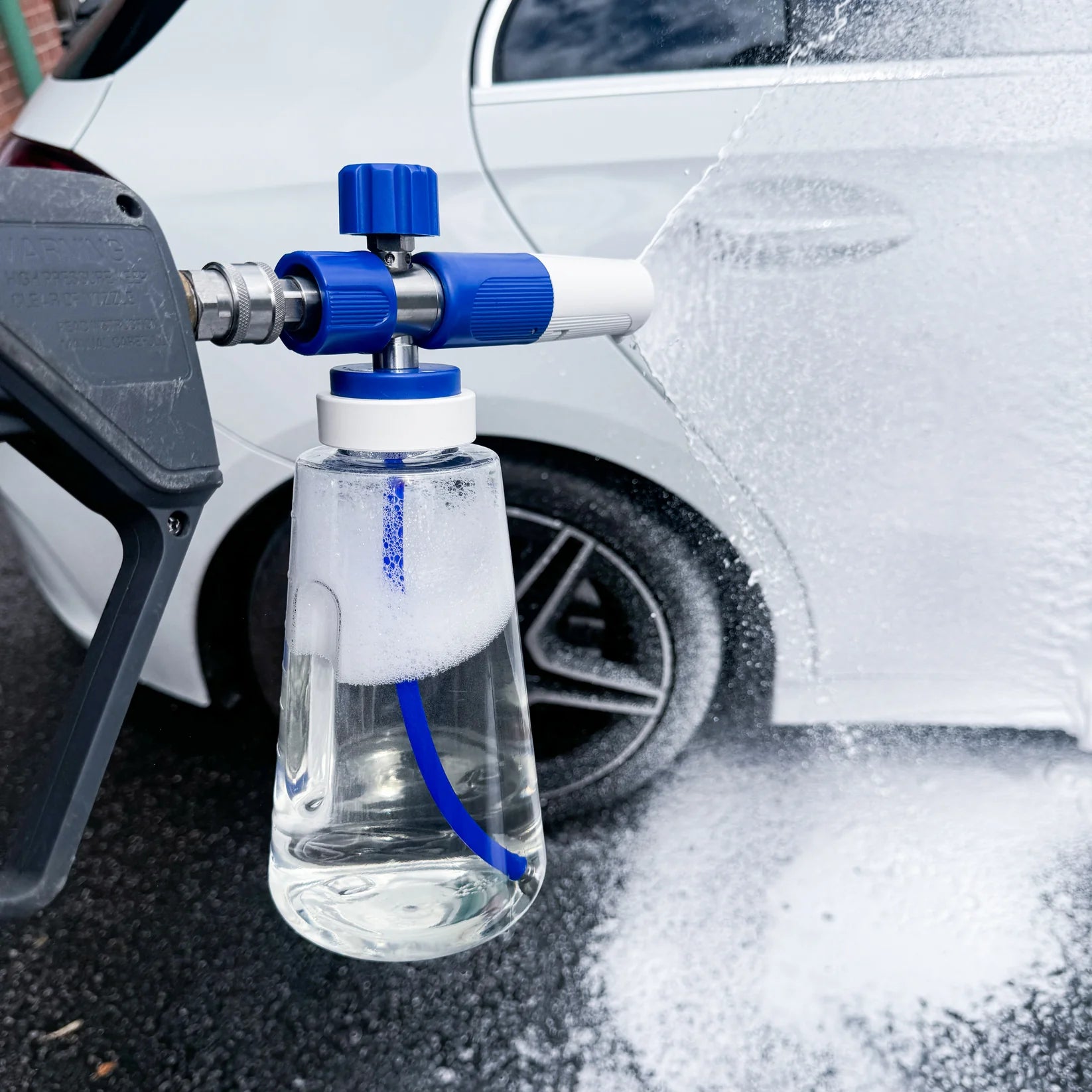 Foam cannon attached to a pressure washer with a car in the background