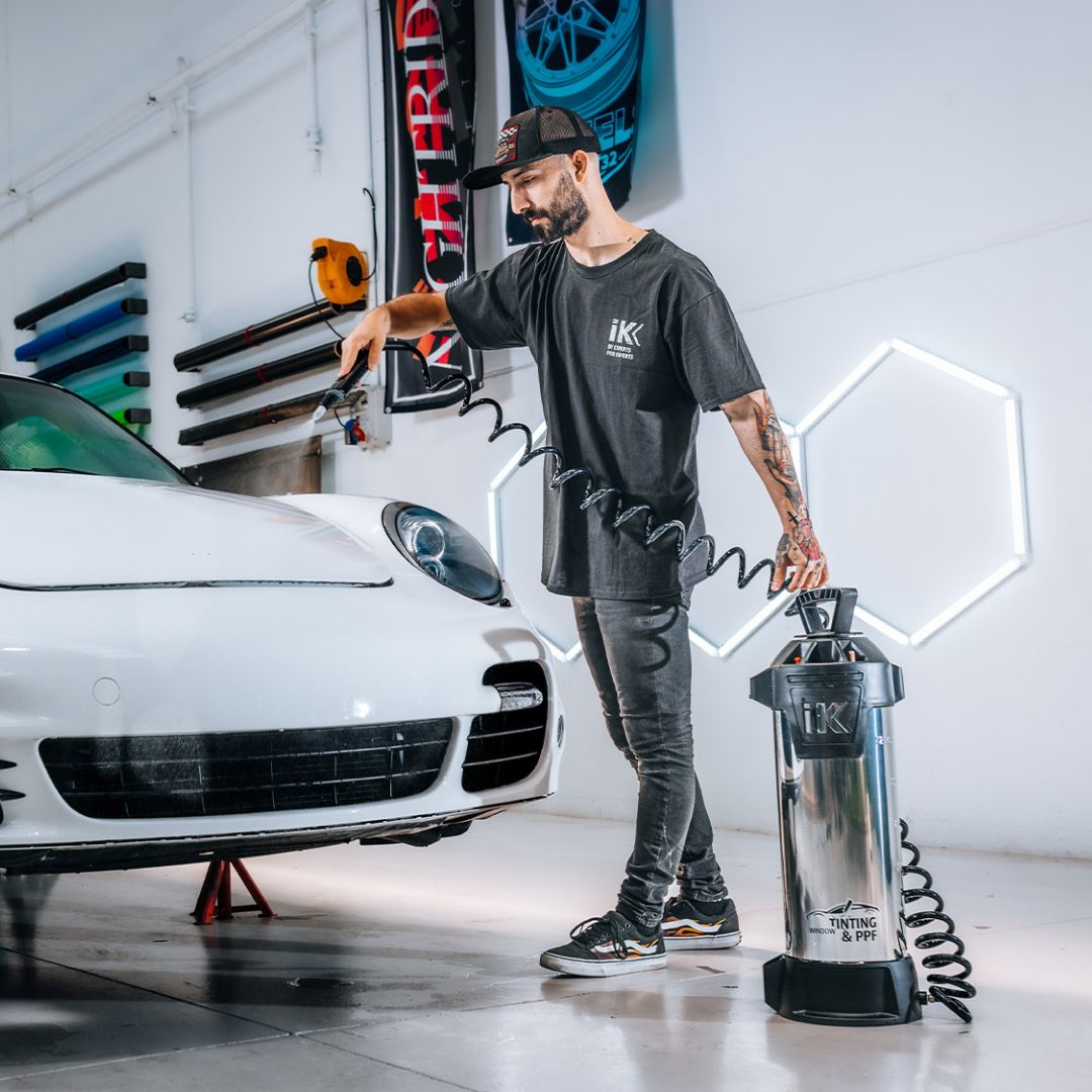 Person holding a cIK Window Tinting and PPF Sprayer Stainless Steel 13L next to a white Porsche 911 Turbo in a garage.
