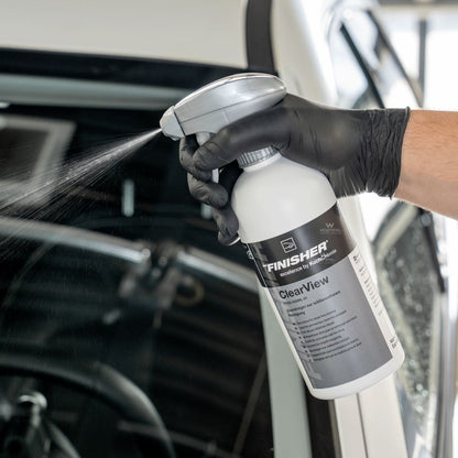 Person using a Koch Chemie 'The Finisher ClearView' Glass Cleaner spray bottle inside a car.