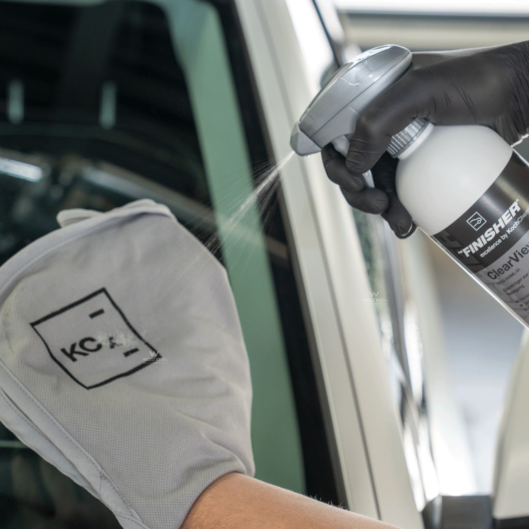 Person wearing gloves and using a Koch Chemie 'The Finisher ClearView' Glass Cleaner on a car window.
