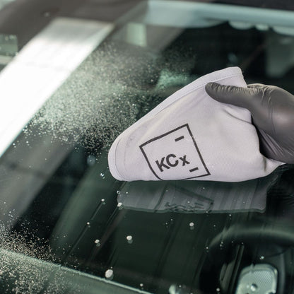 Person cleaning a car window with a white cloth featuring 'KCx' branding.