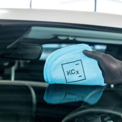 Person cleaning a car's glass with a blue KCX towel.