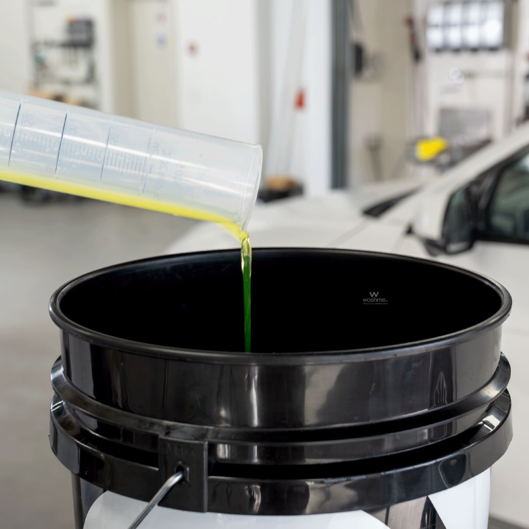 Bottle of Koch Chemie The Finisher TropicSnow being poured from a container into a black oil filter container with a car in the background.