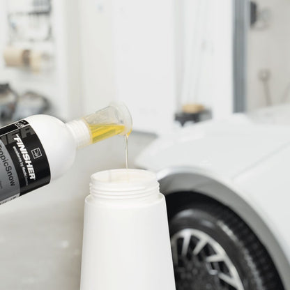 Bottle of Koch Chemie The Finisher TropicSnowbeing poured into a container with a car in the background