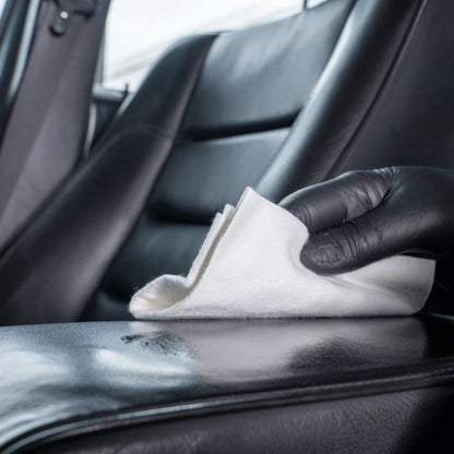Person cleaning a car's black leather seat with a white cloth.