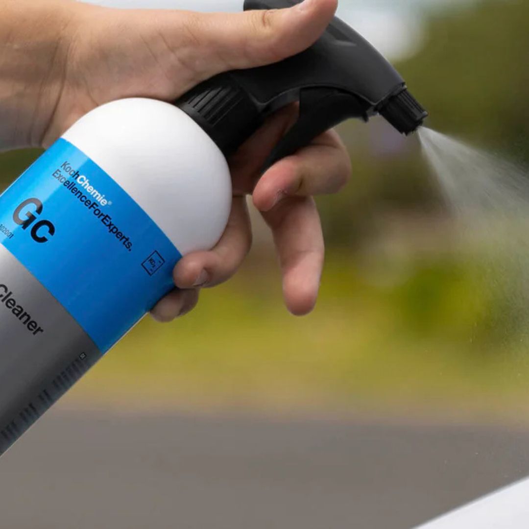 Hand holding a spray bottle labeled 'GC Cleaner' with a blurred outdoor background