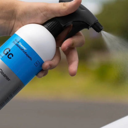 Hand holding a spray bottle labeled 'GC Cleaner' with a blurred outdoor background