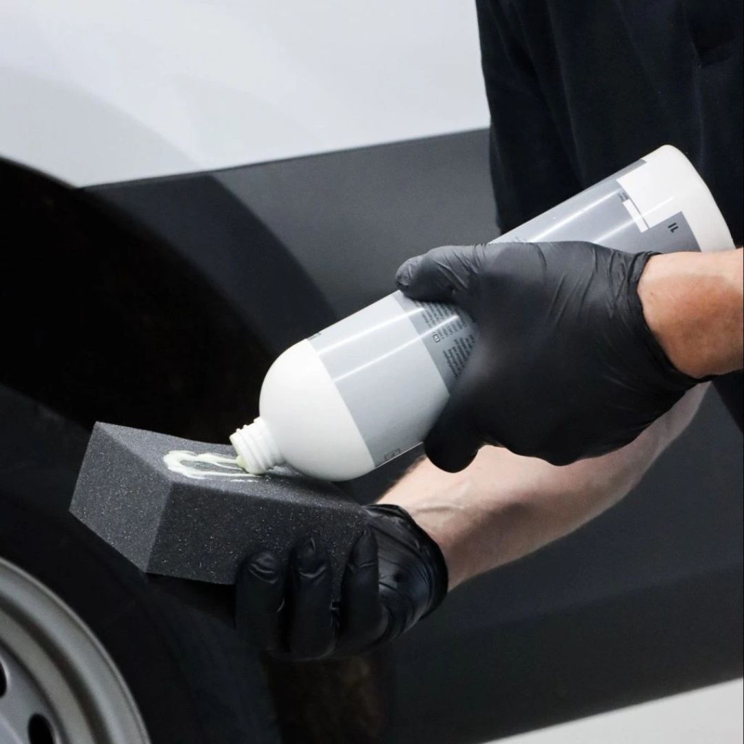 Person applying a Koch Chemie HPC Hydro Plast Care from a bottle onto a black car surface using a gray applicator.