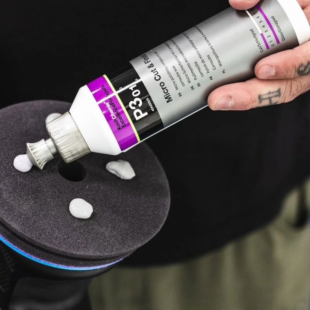 A hand applies a dollop of white Microfiber Wax from a silver tube labeled Koch Chemie Micro Cut & Finish P3.01 polishing compound onto a dark gray foam pad, with more wax dollops visible nearby.