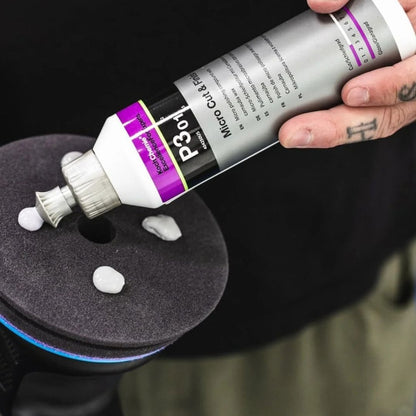 A hand applies a dollop of white Microfiber Wax from a silver tube labeled Koch Chemie Micro Cut & Finish P3.01 polishing compound onto a dark gray foam pad, with more wax dollops visible nearby.