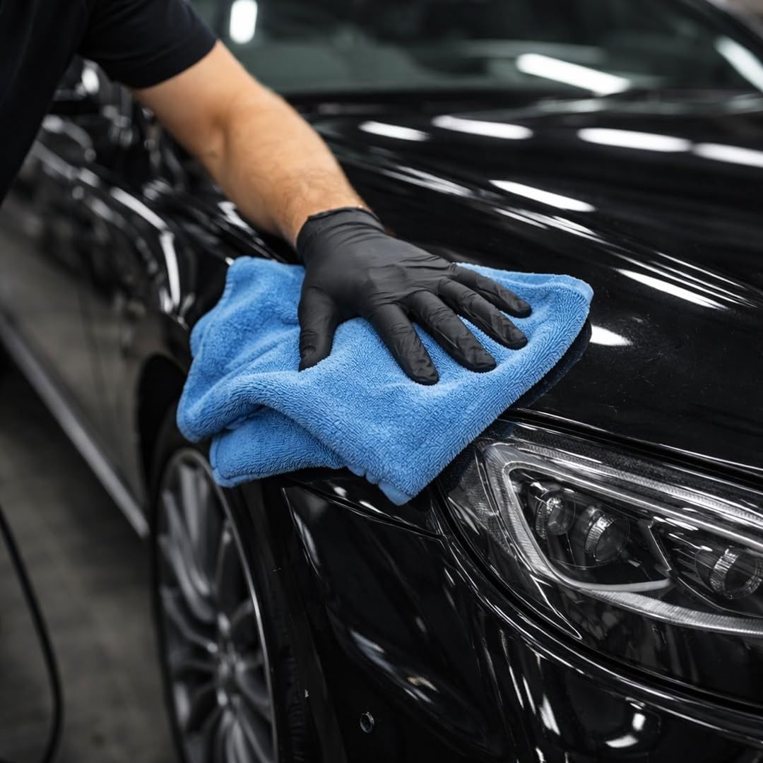 A person with black gloves wiping off Koch Chemie Micro Cut & Finish P3.01 polishing compound from a black Mercedes with a blue soft microfibre cloth