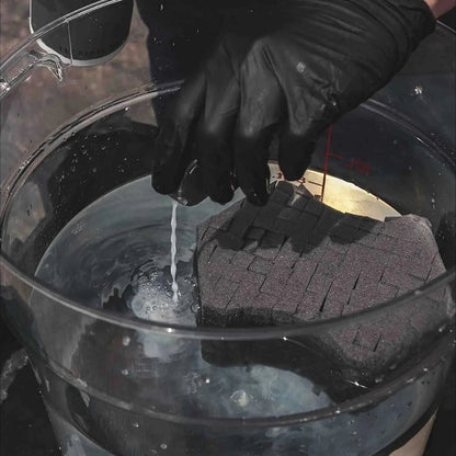 Person wearing a black glove holding a black sponge over a bucket of water.