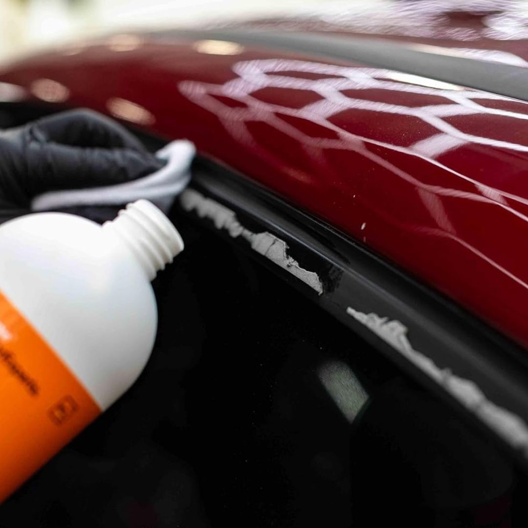 Person applying Koch Chemie Tea to a car's window surrounds with glue residue using a bottle with an orange label.