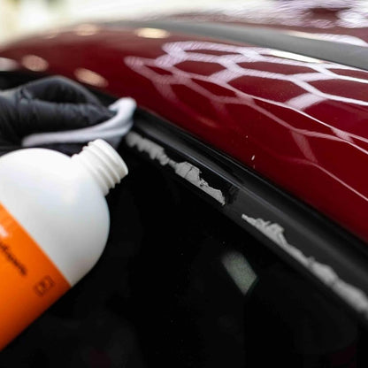 Person applying Koch Chemie Tea to a car's window surrounds with glue residue using a bottle with an orange label.