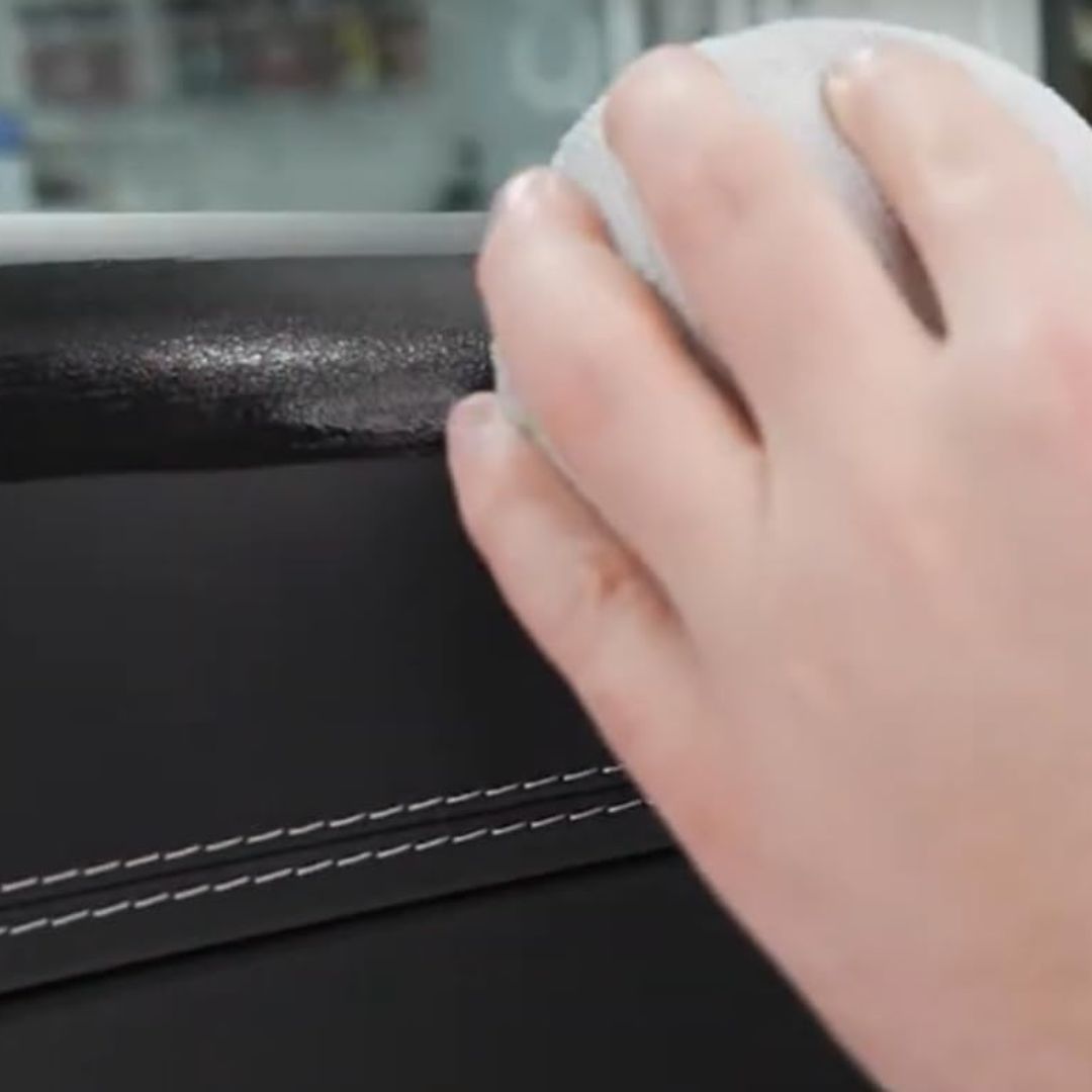 Hand using a white sponge to clean a black surface