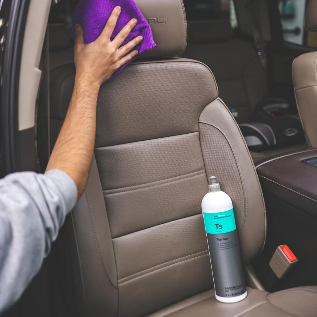 Person cleaning car interior with a Koch Chemie TS Top Star Interior Plastic Cleaner and Dressing bottle and towel