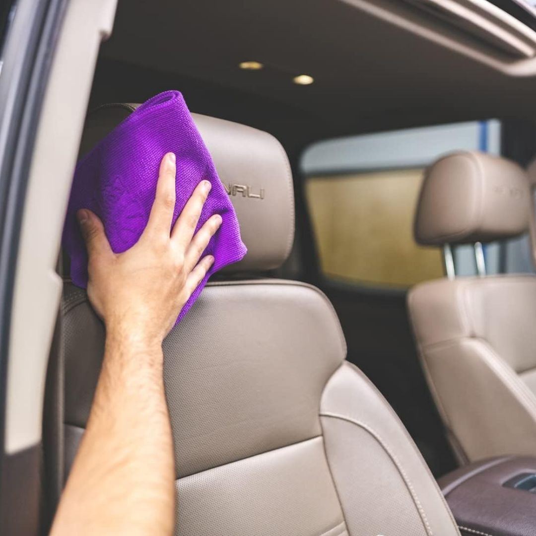 Person cleaning a car seat with a purple towel inside a vehicle.
