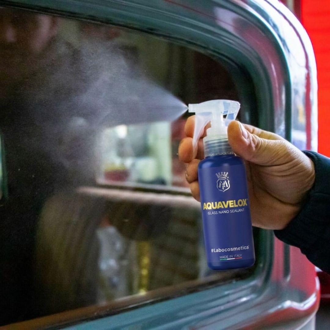 Person holding a blue spray bottle labeled 'Aquavelox' in front of a mirror.