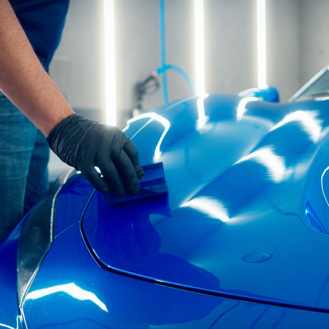 Person applying a protective coating to a blue car using a tool.