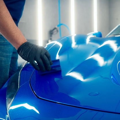 Person applying a protective coating to a blue car using a tool.