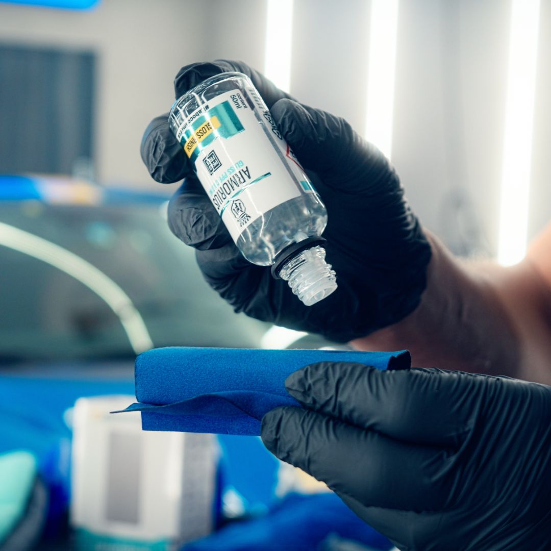 Hand wearing a black glove holding a bottle of alcohol-based hand sanitizer with a blurred background.
