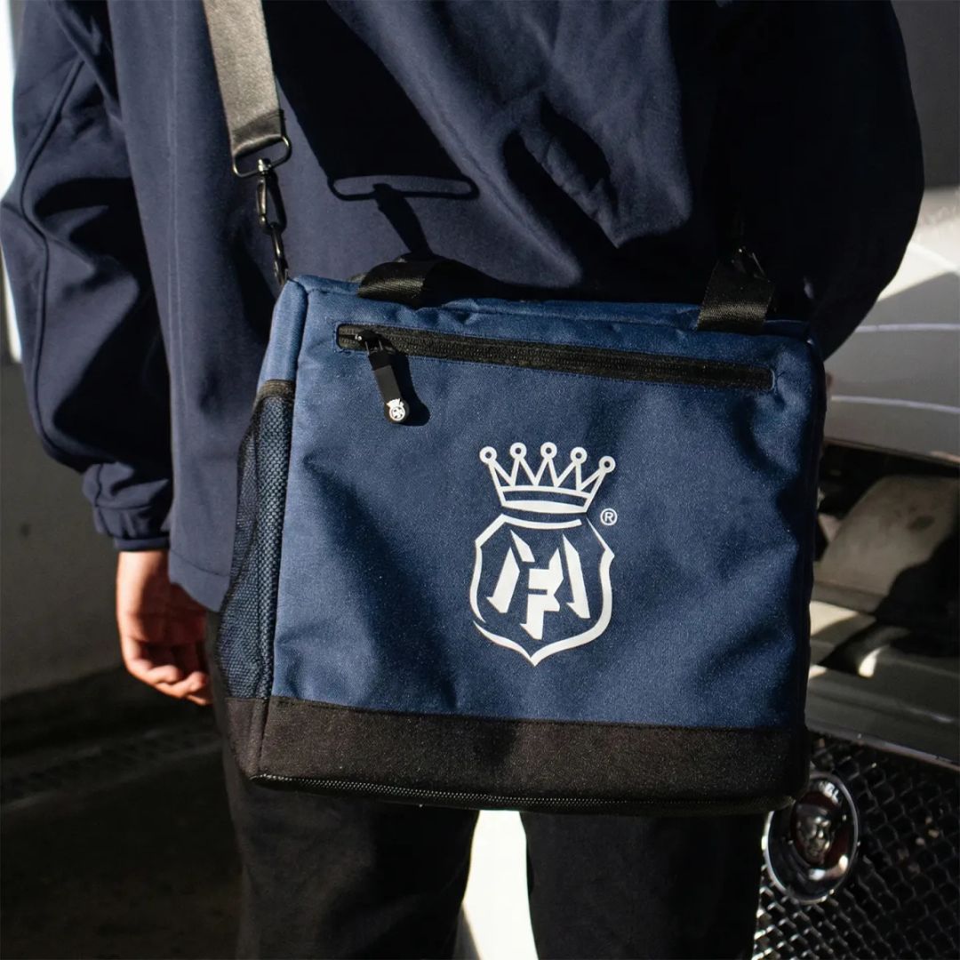 Person holding a navy blue Labocosmetica bag with a logo, standing next to a car.
