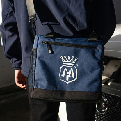 Person holding a navy blue Labocosmetica bag with a logo, standing next to a car.