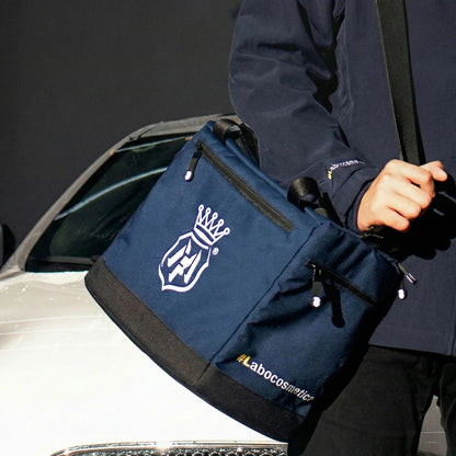 Person holding a navy blue Labocosmetica  bag with a logo and 'Labocosmetica' text next to a car.