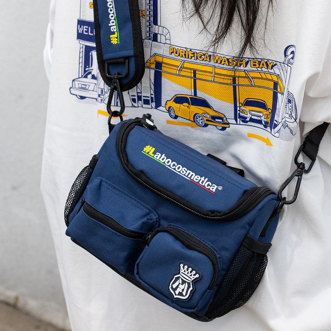 Blue bag with 'labocosmetica' branding worn by a person wearing a graphic t-shirt. Labocosmetica Conibag - Detailing Shoulder Bag (Size S)