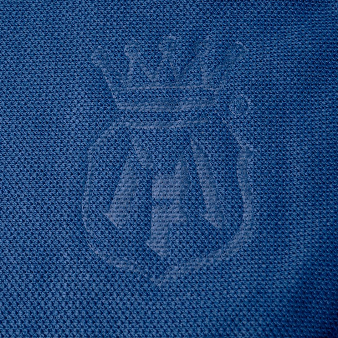 Close-up of a blue textured fabric with a tonal embroidered crest featuring a crown and stylized lettering. Labocosmetica logo