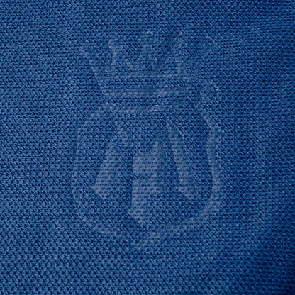 Close-up of a blue textured fabric with a tonal embroidered crest featuring a crown and stylized lettering. Labocosmetica logo