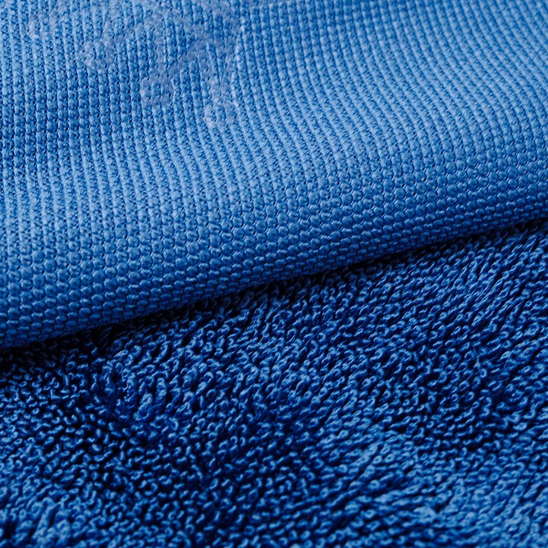 Close-up of a blue microfiber cloth showing its textured surface, with a folded section revealing a plush terry-like underside.